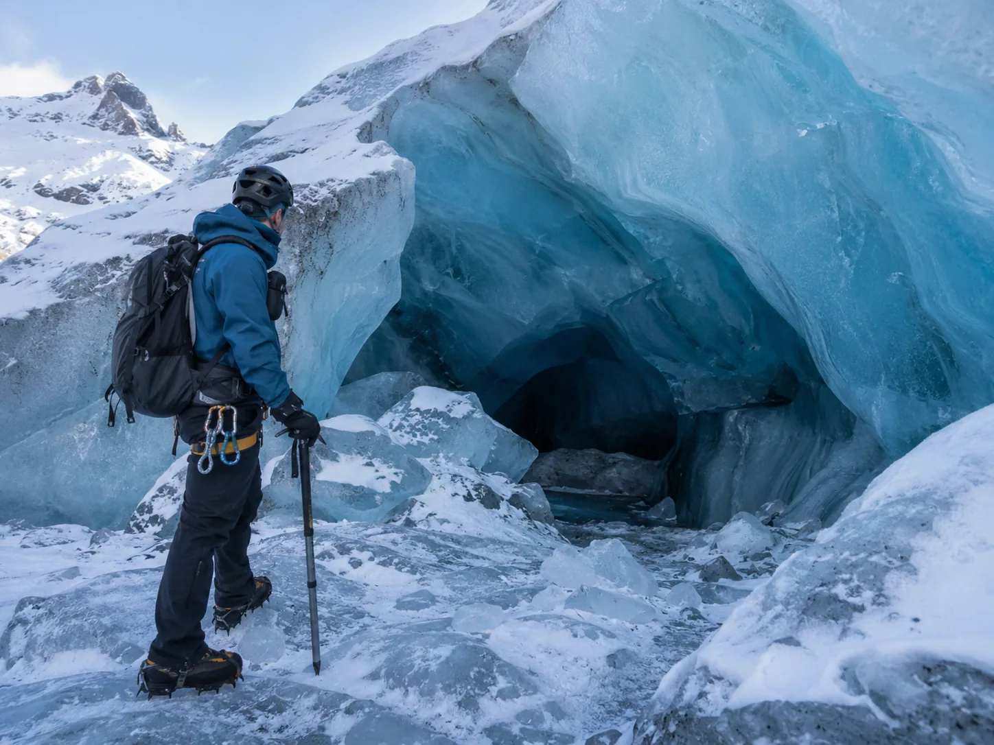 a helmeted visitor beside a glacier opening.